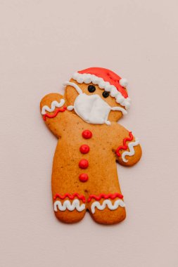 Noel Baba şeklinde kızıl kurabiyelerin koruyucu bir tıbbi maske taktığı fotoğraf.