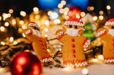 Arka planda odaklanmamış ışıklarla zencefilli kurabiye maskeli adam kurabiyeleri: Koronavirüs salgınında yeni yıl ve Noel kutlaması