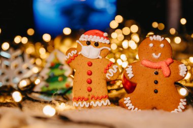 Coronavirus salgını, odaklanmamış ışıklarla kavramsal arka plan Noel süsleri ve koruyucu bir tıbbi maske takan Noel Baba şeklinde zencefilli ekmek.