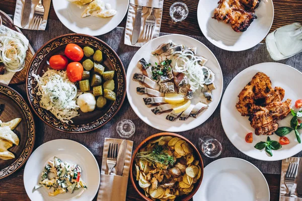 home wooden table covered with plates with various delicious dishes in the Slavic style: sourdough, salted and fried fish, potatoes, fried meat and salads