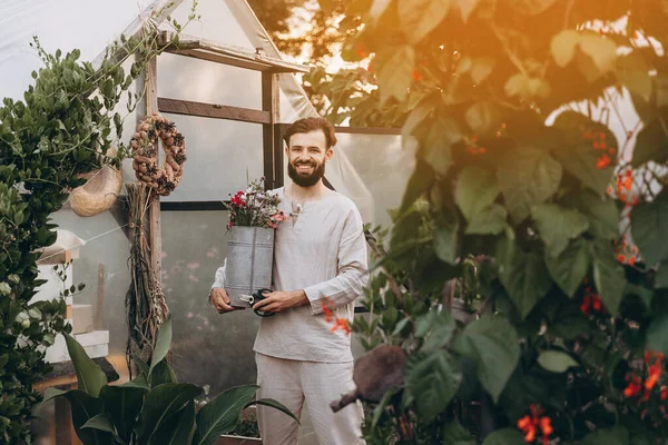 worker in a greenhouse where flowers are grown. Handsome man cares for flowers, flowers for a decor of wedding bouquets to decorate tables in cafes or for gifts, grown in a greenhouse