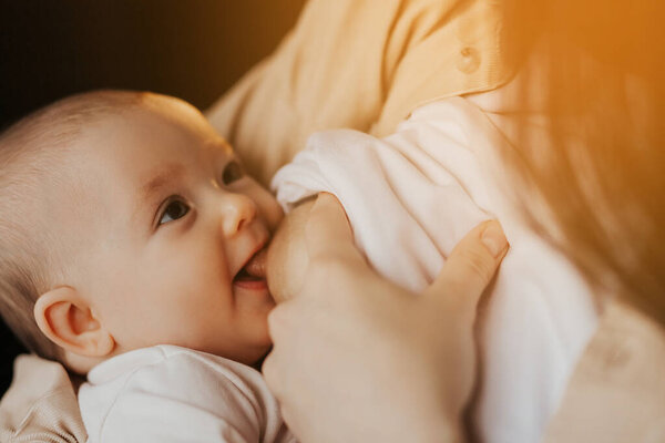 close up portrait of a child breastfeeding. mother breastfeeding smiling baby in bed dark night by lamp light