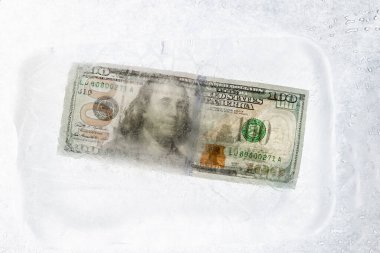 New $ 100 bill frozen under a layer of ice, the concept of the global financial crisis or the fall of the dollar on the world market clipart