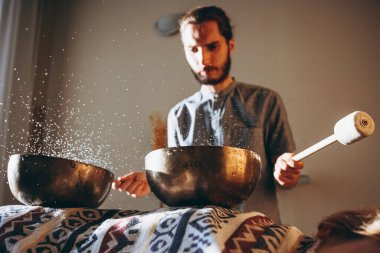 Spa salonunda Nepal Buda bakır kasesi. Genç sakallı adam masaj terapisi yapıyor. Spa 'da şarkı söylüyor. Ses terapisi, dinlenme, meditasyon, sağlıklı konsept.