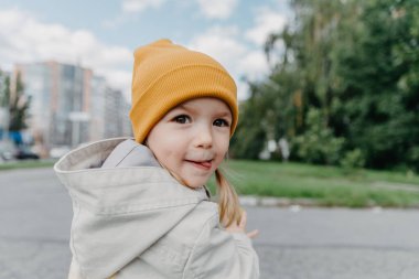Şık bir bahar yağmurluğu ve sarı şapka giymiş bir çocuğun portresi. Yürüyüşe çıkmış mutlu ve neşeli bir bebek 