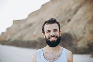 Yüzünde deniz kumu olan sakallı, şık bir gencin portresi.