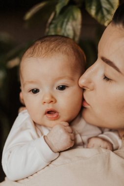 Sevgi dolu anne, yeni doğmuş bebeğini akşam evde taşıyor. Bebek kucağında mutlu bir annenin samimi portresi. Anne 3 aylık kızına sarılıyor.