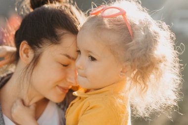 Genç esmer anne, kıvırcık kızını tutuyor.