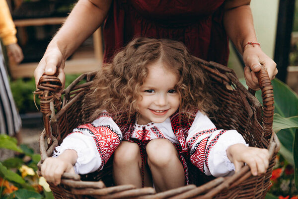 Portrait of a cute curly girl dressed in Ukrainian folk embroidered dress posing for a photo in the garden with flowers