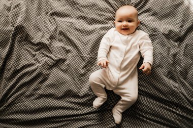 Odadaki yatakta uzanıp oynayan, pencereden gün ışığıyla çekilmiş güzel bir bebek.