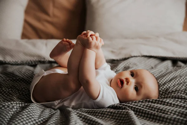 Niño Feliz Acostado Cama Sosteniendo Sus Piernas — Foto de Stock