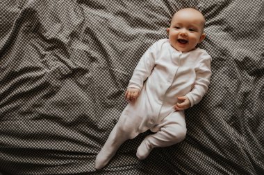 Odadaki yatakta uzanıp oynayan, pencereden gün ışığıyla çekilmiş güzel bir bebek.