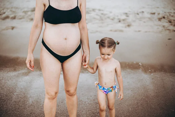 海のそばの水着に身を包んだ女の子と妊婦さん 幸せな家族の休暇の本当の写真 水の中に立つお父さんの写真 — ストック写真