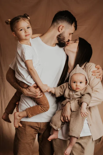 スタイリッシュなひげを生やした父親とかわいい妻がかわいい子供たちを腕に抱えている若い誠実な家族 スタジオでの家族写真撮影 — ストック写真