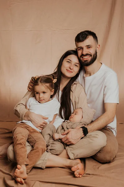 スタイリッシュなひげを生やした父親とかわいい妻がかわいい子供たちを腕に抱えている若い誠実な家族 スタジオでの家族写真撮影 — ストック写真