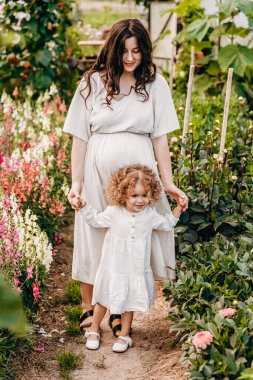 Güzel kıvırcık kız annesiyle güneşli parkta yürüyor. Açık havada yaz tatili kavramı. Anneler günü, bebekler günü. Birlikte vakit geçirmek.