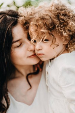 Güzel kıvırcık kız annesiyle güneşli parkta yürüyor. Açık havada yaz tatili kavramı. Anneler günü, bebekler günü. Birlikte vakit geçirmek.