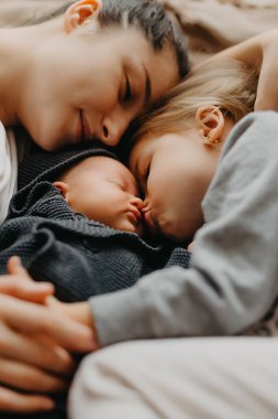 Anne, kızlarının yanında uyumak için uzandı. Anneleriyle sarılıp uyuyan çocukların ev fotoğrafı.