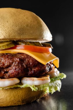 Pirzola, salata, peynir ve yenilebilir altın boyayla boyanmış karidesli sulu bir hamburger fotoğrafı.