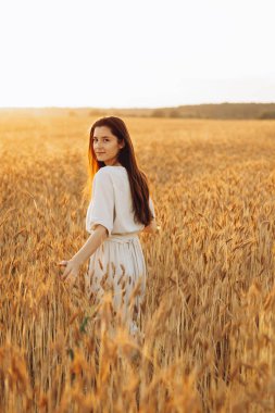 Çekici Ukraynalı uzun saçlı, ince ve güzel bir kız sarı güneşli bir tarlada buğdaylı fotoğraf için poz veriyor.