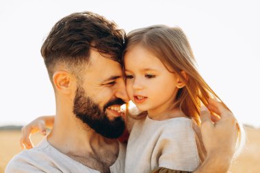 Babasının kollarında tatlı küçük bir kız. Baba ve kızı güneşli bir yaz gününde parkta eğleniyorlar. Babası tarafından tutulan sevimli bir çocuk.