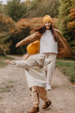 Genç, mutlu ve gülümseyen bir anne ve kucağında küçük kızı, bir sonbahar parkında yürüyüş yaparken sarılıp öpüşüyorlar. seçici odak, gürültü etkisi, sonbahar havası
