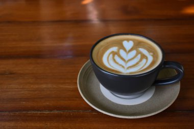 Üzerinde latte resmi olan sıcak bir latte fincanı ahşap masaya konur.. 