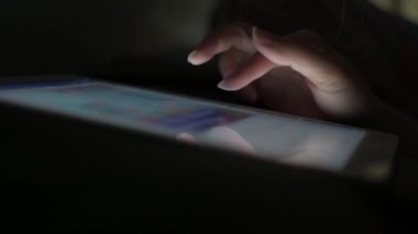 Bir kadının parmağı bir tabletin ekranından kayıp sosyal medyada oynamak için ışığı açmadan uykuya dalmadan önce yatakta kayar..
