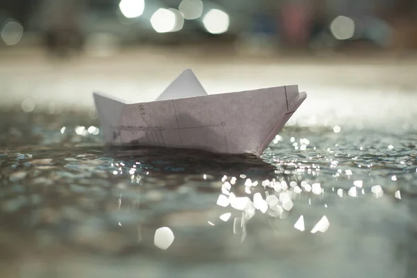 A snow-white paper boat, made of documents, floats in the spring on a puddle in the city