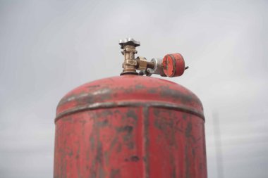 Bulutlu gökyüzünün arka planına karşı kırmızı renkli bir gaz silindiri. Çatıda eski döküntüler var.