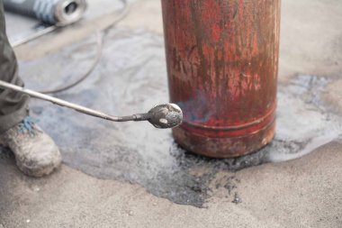 Bir işçi gaz tüpünü eski bir iş ayakkabısında açık bir ateşle ısıtır. Gaz basıncını artırmak için güvenlik yönetmeliklerinin ihlali.