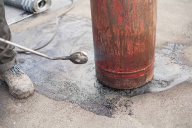 Bir işçi gaz tüpünü eski bir iş ayakkabısında açık bir ateşle ısıtır. Gaz basıncını artırmak için güvenlik yönetmeliklerinin ihlali.