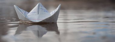 Bir su birikintisinde yüzen, defter çarşafından beyaz bir tekne.