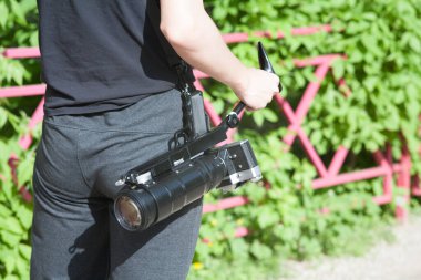 Kamera kemerde, fotoğrafçı dikiz aynası, fotoğrafçı yeşil yeşillik ve kırmızı çitin arka planında.