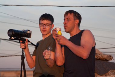 Baba ve oğul batan güneşin altında yüksek bir binanın çatısında oynaşıyorlar. Bir adam ve bir genç gün batımında çatıda iletişim kablolarıyla çevrili. İnsanların günbatımı telleri Akşam gökyüzü iletişimi