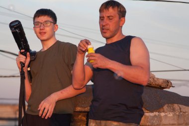 Baba ve oğul batan güneşin altında yüksek bir binanın çatısında oynaşıyorlar. Bir adam ve bir genç gün batımında çatıda iletişim kablolarıyla çevrili. İnsanların günbatımı telleri Akşam gökyüzü iletişimi