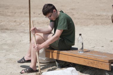 Gençler şehir plajında çöp toplamakla meşgul. Sıcak yazda gölde temizlik yapmak. Temizlik beyaz çöp torbasına çivi çakılmış bir sopayla yapılır..