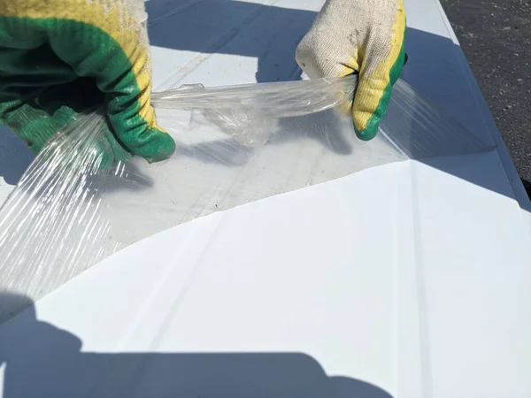 Removing the protective film from the tin part of the facade painted in white. Carefully remove the protective film with the fingers of gloved hands. The fingers of the hands remove the film. The concept is a neat job.
