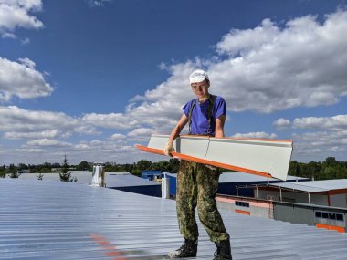 Yazın, güneşli bir günde binanın çatısında çatı tamiratı yapan adam.