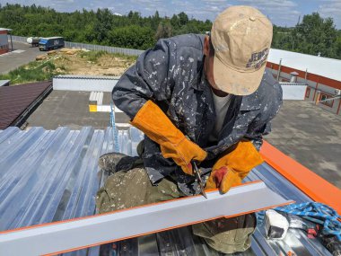 Yazın, güneşli bir günde binanın çatısında çatı tamiratı yapan adam.