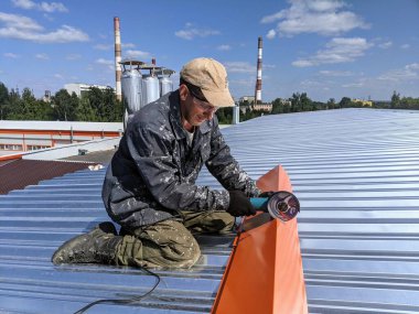 Yazın, güneşli bir günde binanın çatısında çatı tamiratı yapan adam.