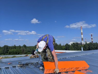 Yazın, güneşli bir günde binanın çatısında çatı tamiratı yapan adam.