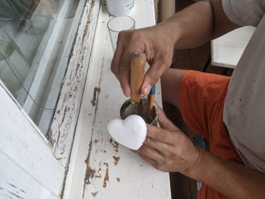 Adamın biri evdeki balkonun pencere eşiğinde otururken oyuncak yapıyor.