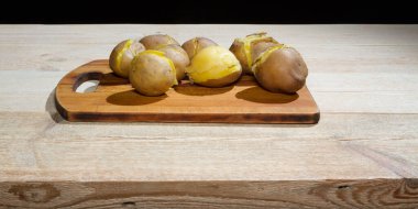 Tahta bir masada kabukta pişirilmiş patatesler. Yeşil soğan, salatalık turşusu.