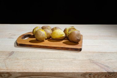 Tahta bir masada kabukta pişirilmiş patatesler. Yeşil soğan, salatalık turşusu.