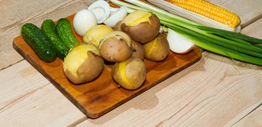 Tahta bir masada kabukta pişirilmiş patatesler. Yeşil soğan, salatalık turşusu, mısır, haşlanmış yumurta.