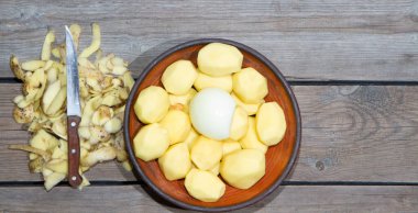 Eski ahşap bir masada patates pişirmek. Tahta bir masada, sarı bir tencerede çiğ patates. Eski tahta tahtalar ve sebzeler.