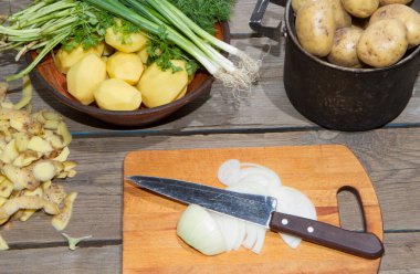 Eski ahşap bir masada patates pişirmek. Tahta bir masada, sarı bir tencerede çiğ patates. Eski tahta tahtalar ve sebzeler.