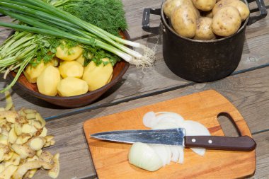 Eski ahşap bir masada patates pişirmek. Tahta bir masada, sarı bir tencerede çiğ patates. Eski tahta tahtalar ve sebzeler.