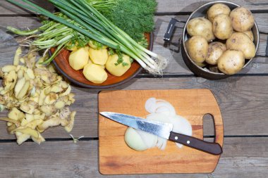 Eski ahşap bir masada patates pişirmek. Tahta bir masada, sarı bir tencerede çiğ patates. Eski tahta tahtalar ve sebzeler.